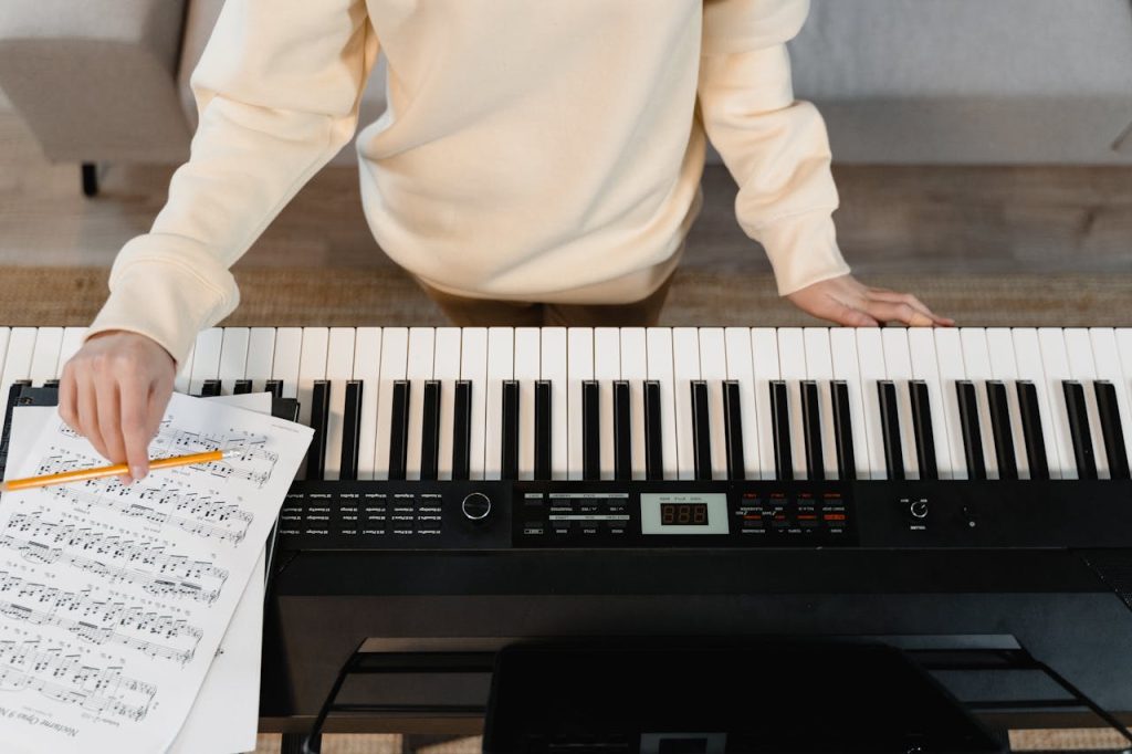 Person studying music with piano and sheets, focusing on practice.